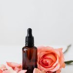 Elegant dropper bottle with pink rose petals on a wooden plate, perfect for aromatherapy or skincare.