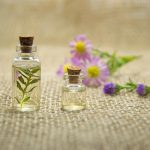 Glass bottles with essential oils and fresh flowers on burlap fabric creating a natural aroma.